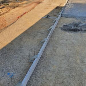 Bordure d'un coffrage au sol sur sol gravier, avec filets rubalise oranges tout autour.